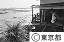 多摩川の氾濫で家のすぐ下を流れる水を見る人