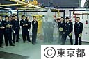 消火設備実習室で、教官からスプリンクラーの説明を聞く学生達